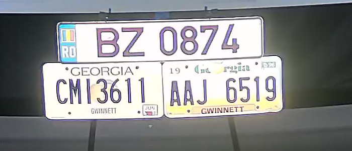 100 percent crop from the COXPAL A17D front camera of three license plates under a spotlight beside the lens, every character legible