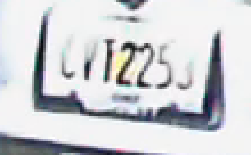 A Jeep's rear license plate at night at eight times enlargement with HDR off: the plate face is washed to white and only some characters survive as thin dark fragments