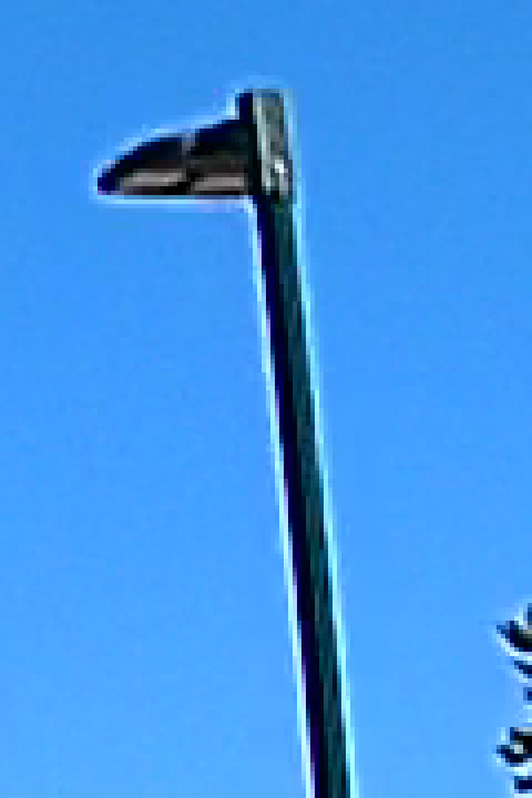 A light pole against a clear blue sky at four times enlargement with HDR off, a bright white line running along both edges of the dark pole